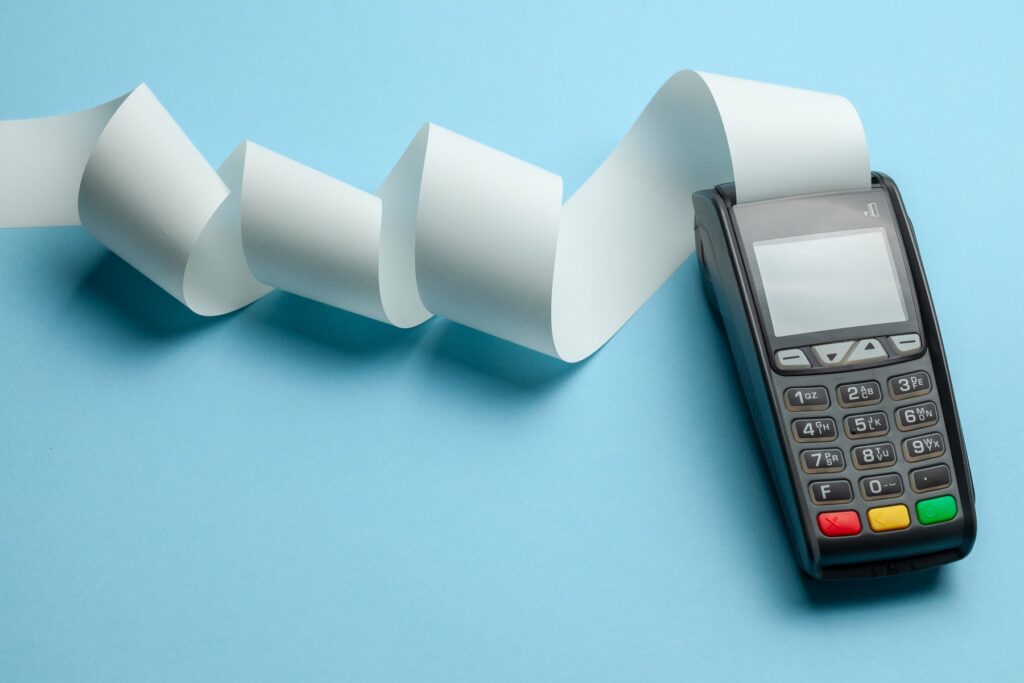 Terminal cash register machine POS for payments and long roll cash tape on blue background. Copy space for text. dragan/AdobeStock